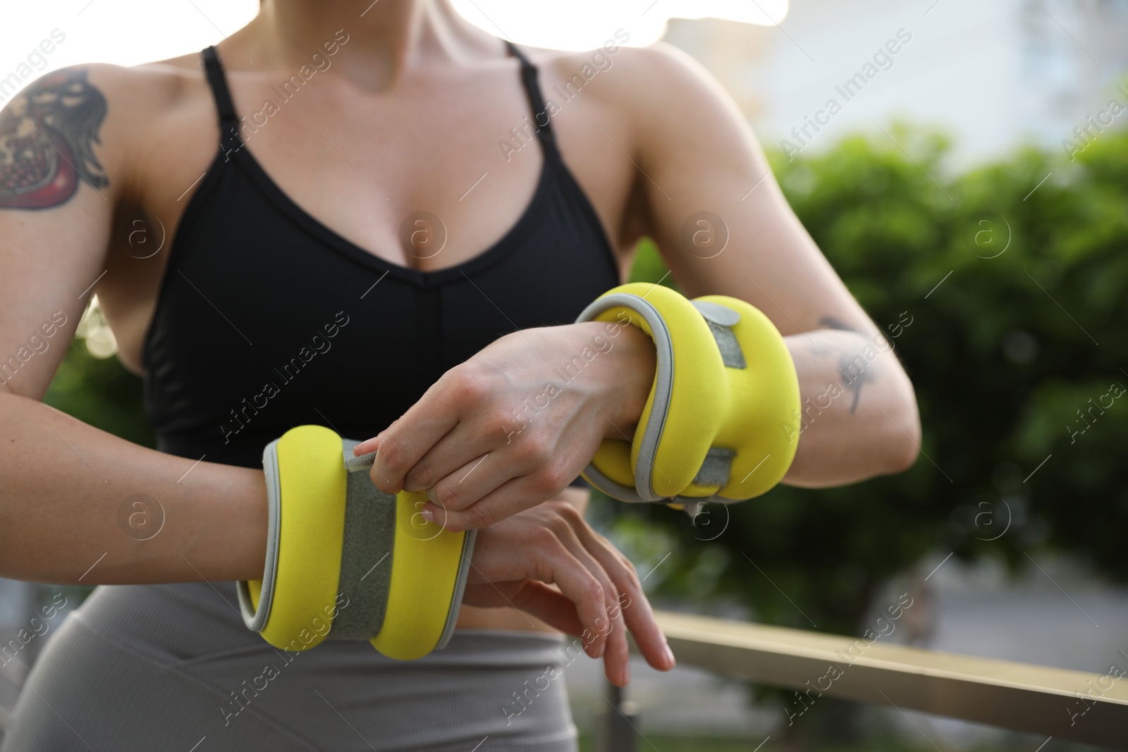 Photo of Woman putting ankle weight on her arm outdoors, closeup