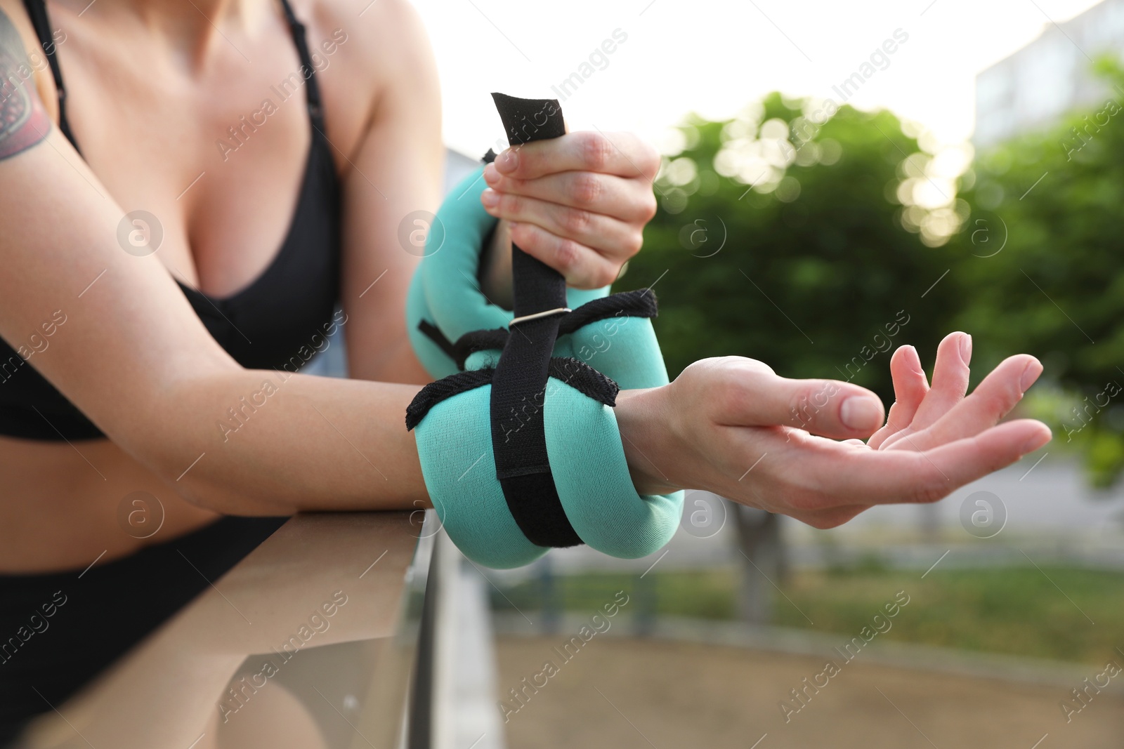 Photo of Woman putting ankle weight on her arm outdoors, closeup