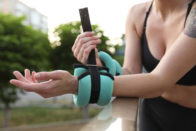 Woman putting ankle weight on her arm outdoors, closeup