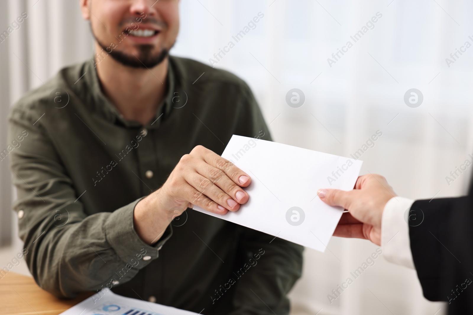 Photo of Smiling employee receiving envelope with salary from boss in office, closeup