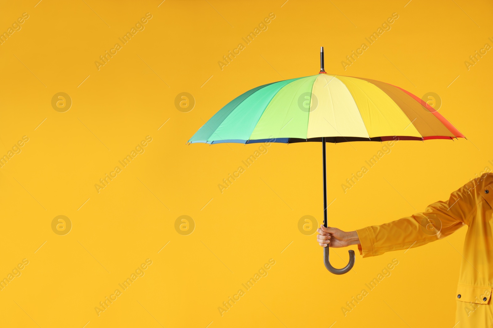 Photo of Woman with colorful umbrella on yellow background, closeup. Space for text