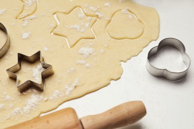 Photo of Raw dough, cookie cutters and rolling pin on white table, closeup