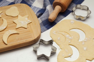 Photo of Raw dough, cookie cutters and rolling pin on white table, closeup