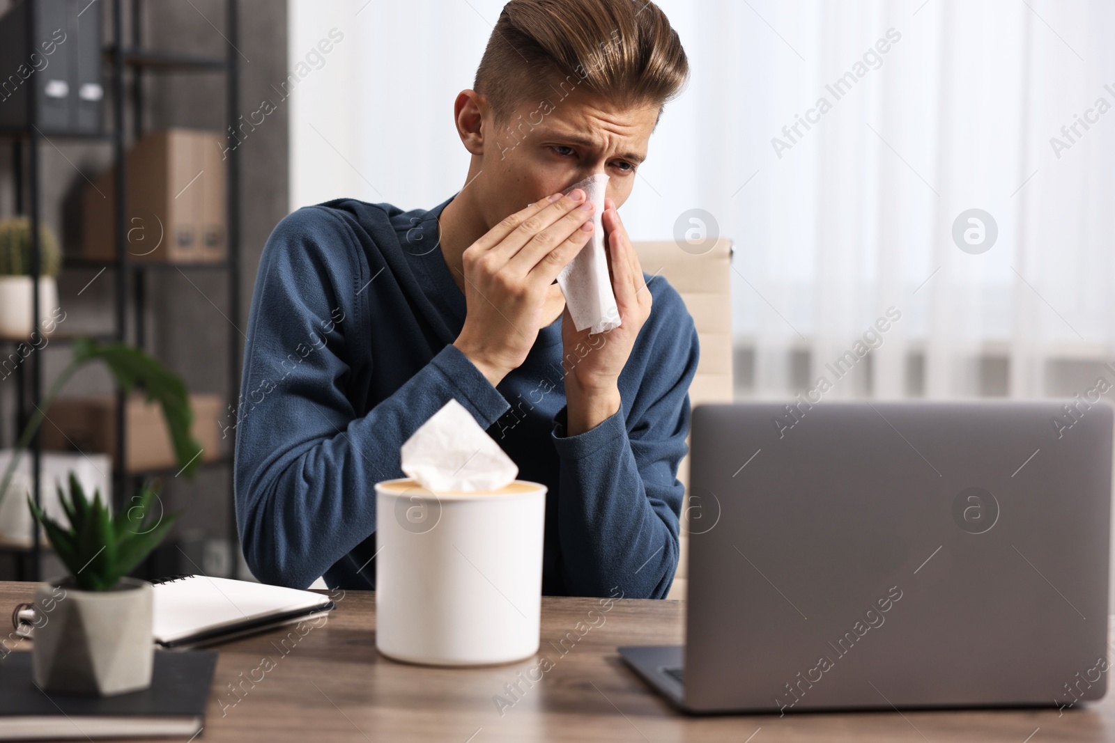 Photo of Young man with tissue suffering from sinusitis at wooden table indoors