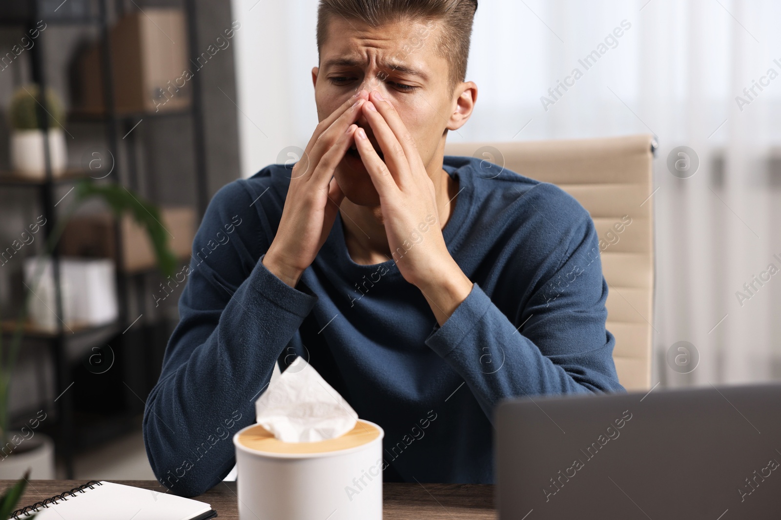 Photo of Young man with tissue suffering from sinusitis at wooden table indoors