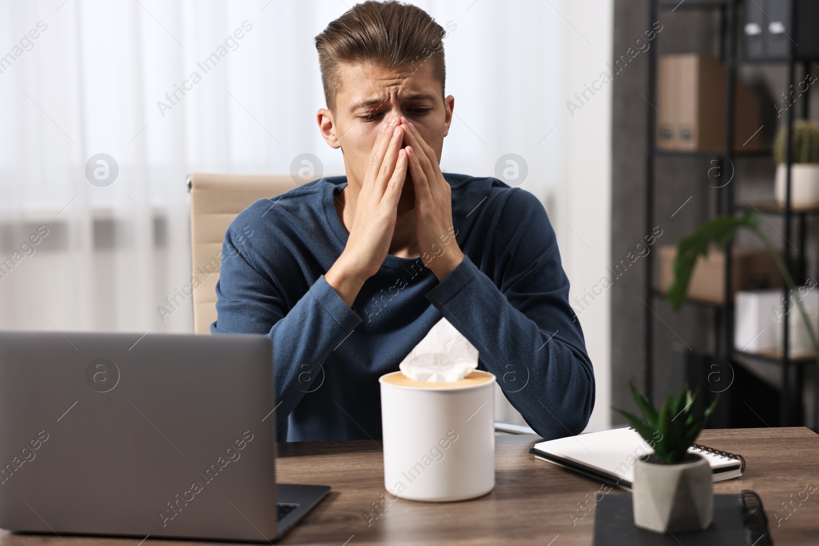 Photo of Young man with tissue suffering from sinusitis at wooden table indoors