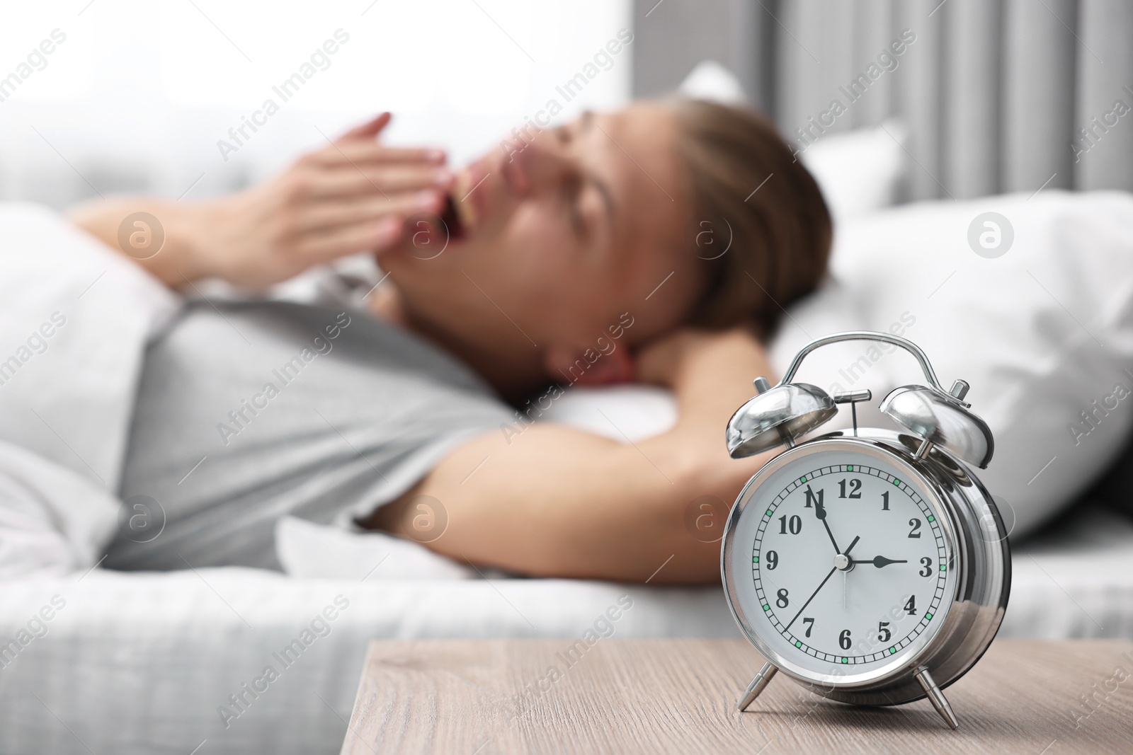 Photo of Man waking up in bedroom at lunch time, focus on alarm clock