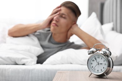 Photo of Man waking up in bedroom at lunch time, focus on alarm clock