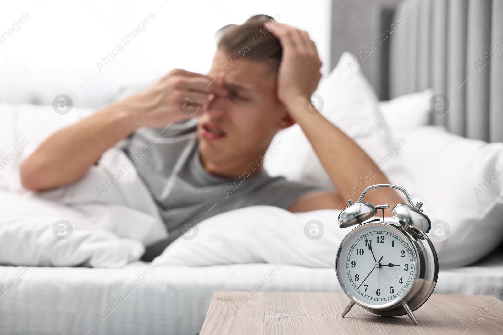 Photo of Man waking up in bedroom at lunch time, focus on alarm clock