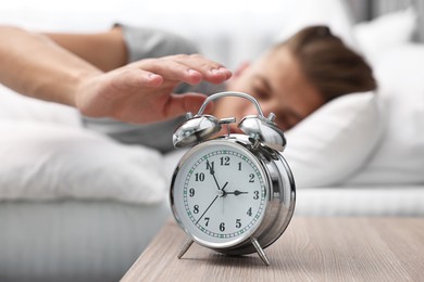 Photo of Man turning off alarm clock in bedroom at lunch time, selective focus