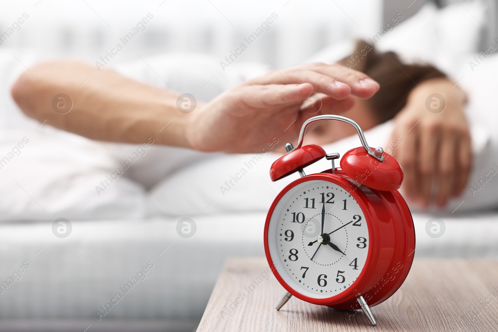 Photo of Man turning off alarm clock in bedroom at lunch time, selective focus