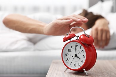 Man turning off alarm clock in bedroom at lunch time, selective focus