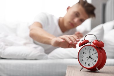 Man turning off alarm clock in bedroom at lunch time, selective focus