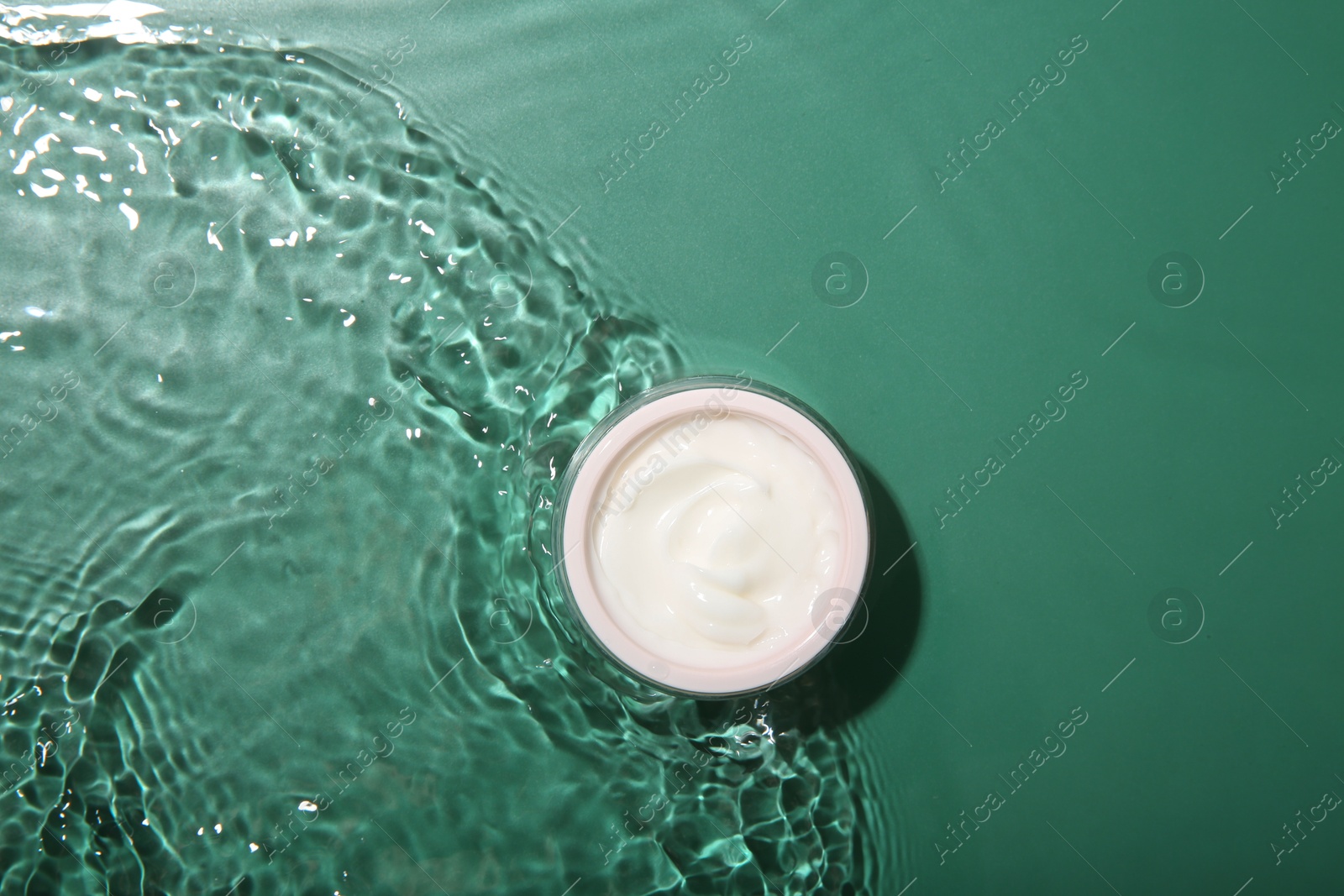 Photo of Cosmetic product. Jar with cream in water on green background, top view