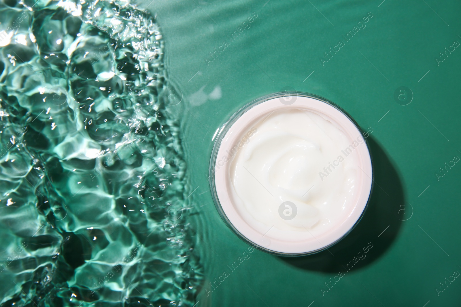 Photo of Cosmetic product. Jar with cream in water on green background, top view. Space for text