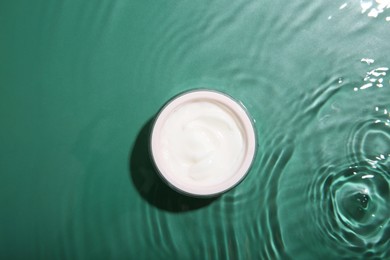 Photo of Cosmetic product. Jar with cream in water on green background, top view