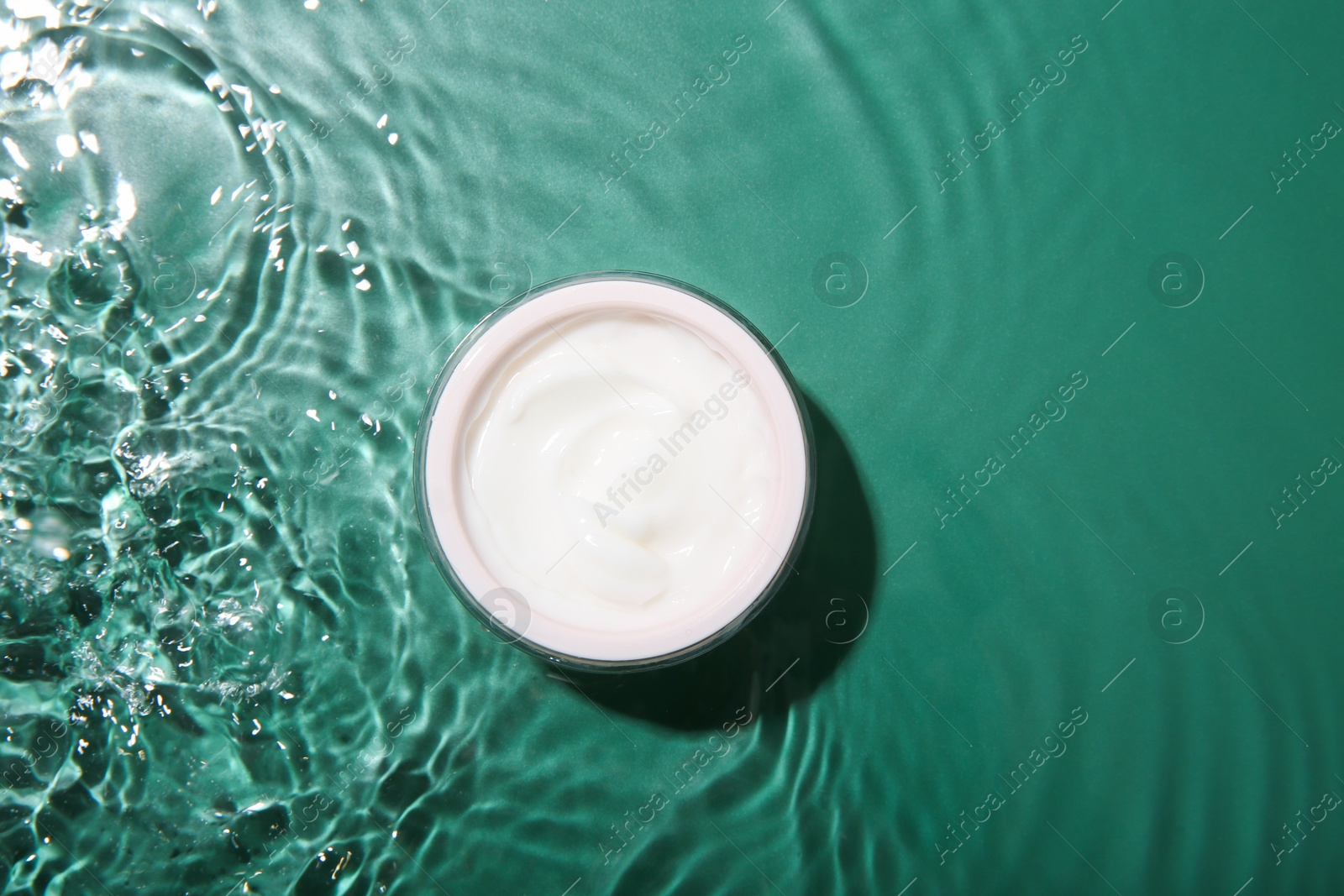 Photo of Cosmetic product. Jar with cream in water on green background, top view