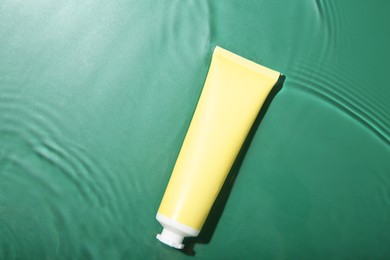 Cosmetic product. Tube with cream in water on green background, top view