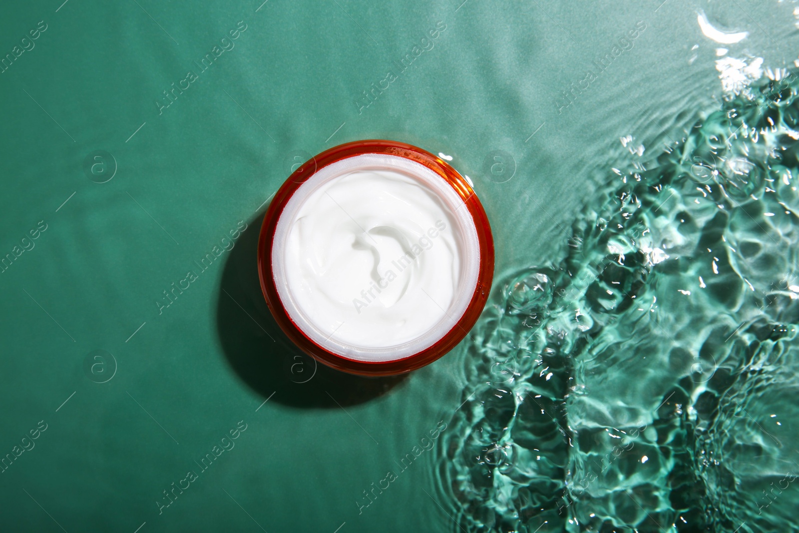 Photo of Cosmetic product. Jar with cream in water on green background, top view