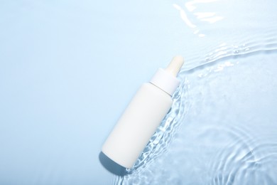 Bottle of cosmetic product in water on light blue background, top view