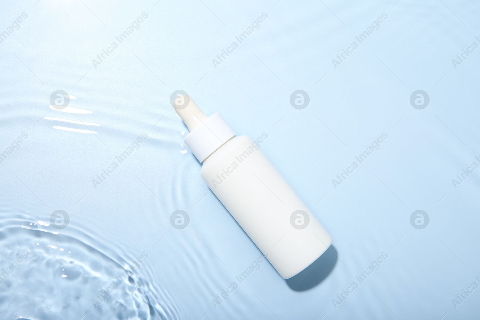 Photo of Bottle of cosmetic product in water on light blue background, top view