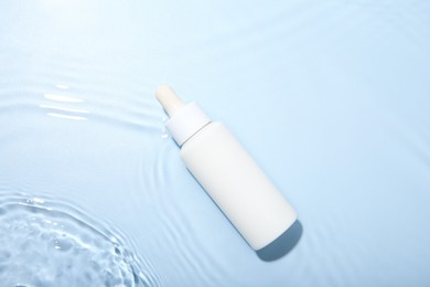 Bottle of cosmetic product in water on light blue background, top view