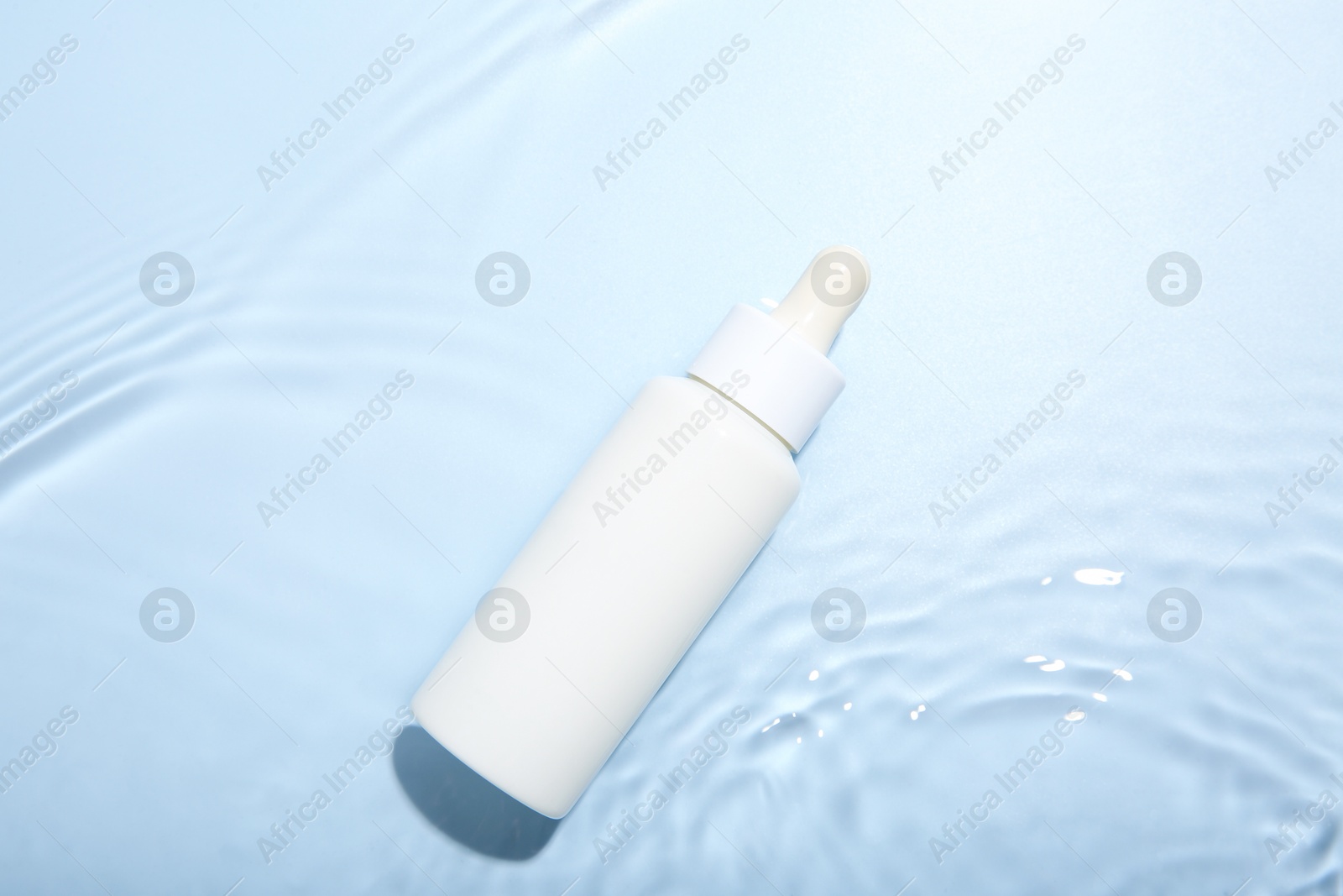 Photo of Bottle of cosmetic product in water on light blue background, top view