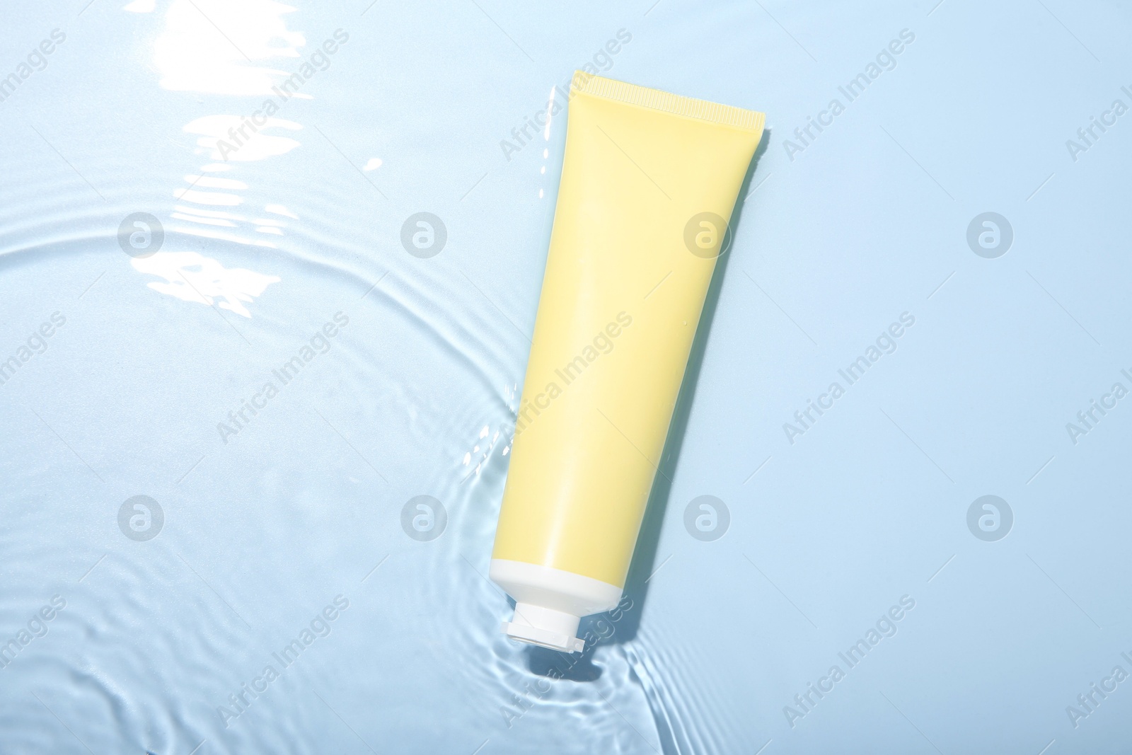 Photo of Cosmetic product. Tube with cream in water on light blue background, top view