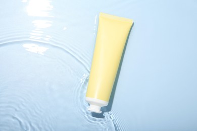 Cosmetic product. Tube with cream in water on light blue background, top view