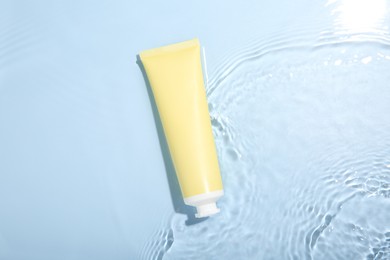 Cosmetic product. Tube with cream in water on light blue background, top view