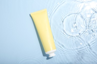 Cosmetic product. Tube with cream in water on light blue background, top view