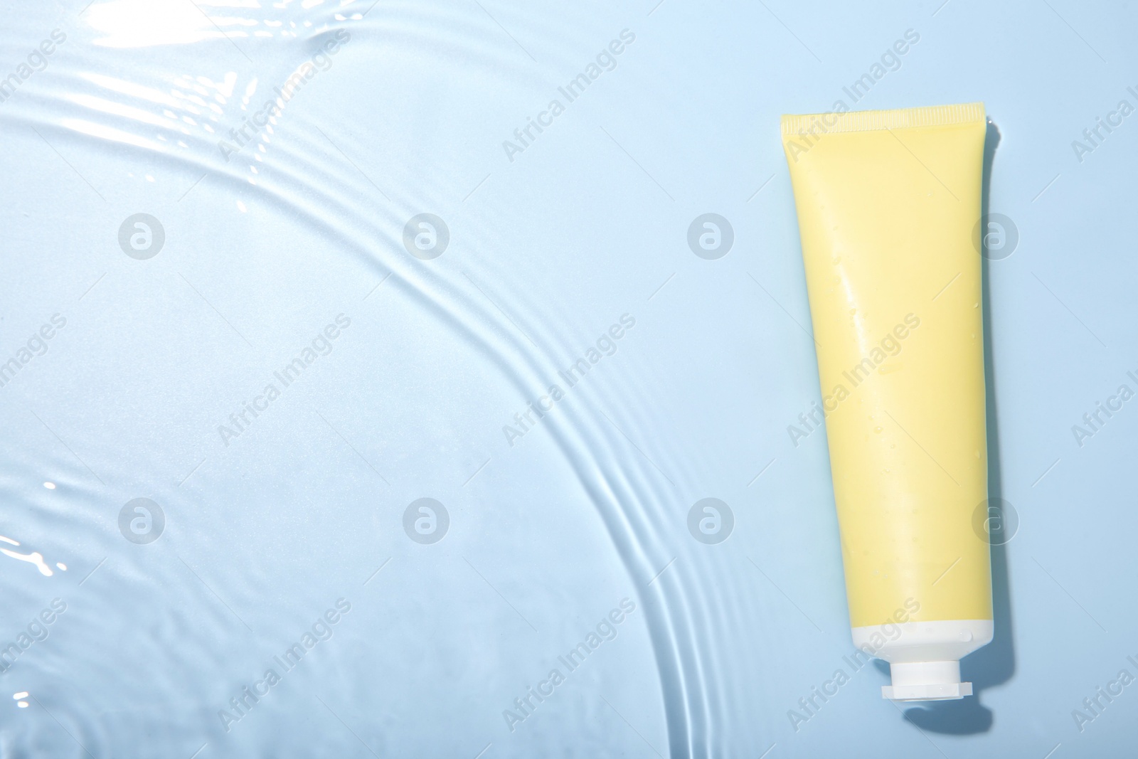 Photo of Cosmetic product. Tube with cream in water on light blue background, top view. Space for text