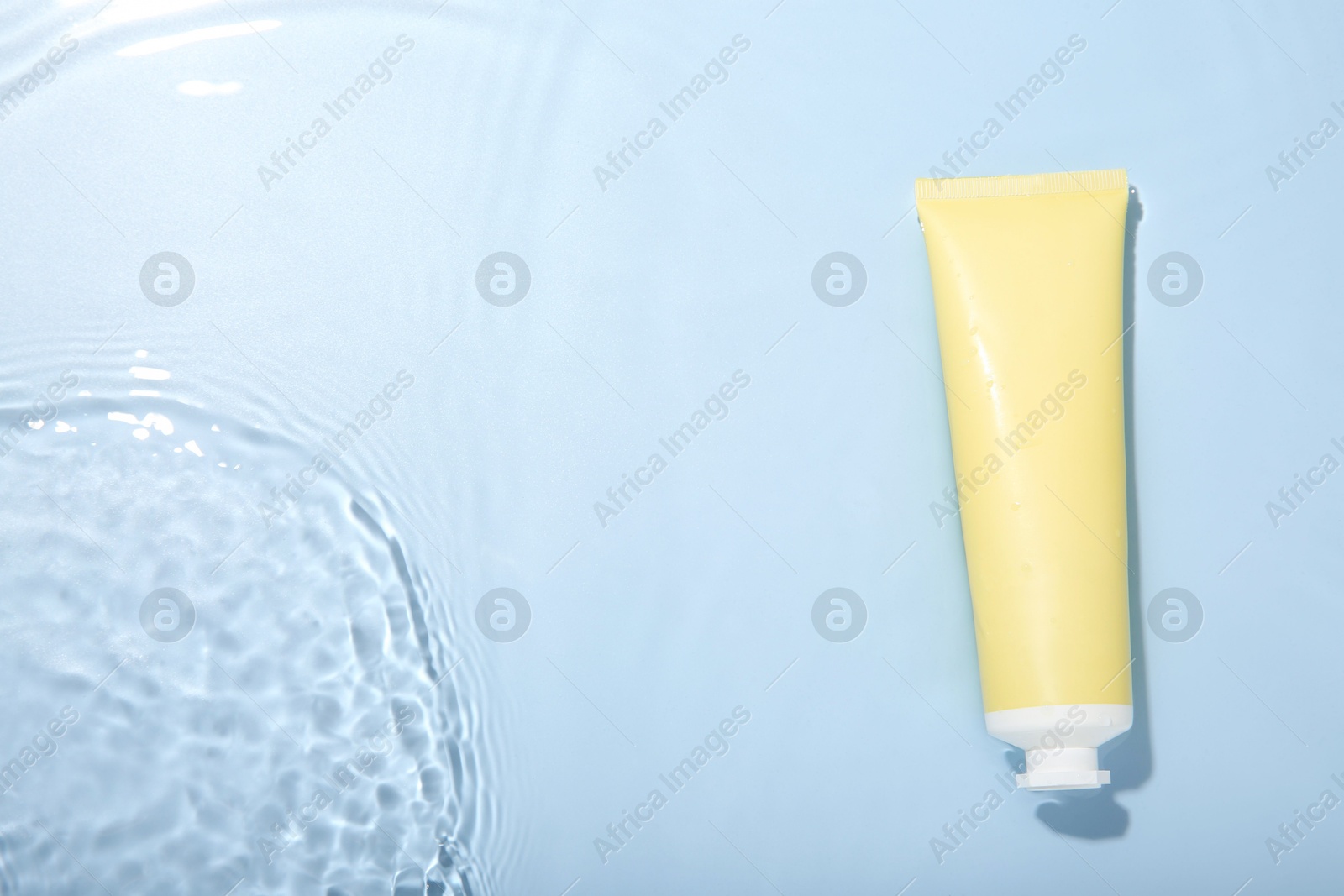 Photo of Cosmetic product. Tube with cream in water on light blue background, top view. Space for text