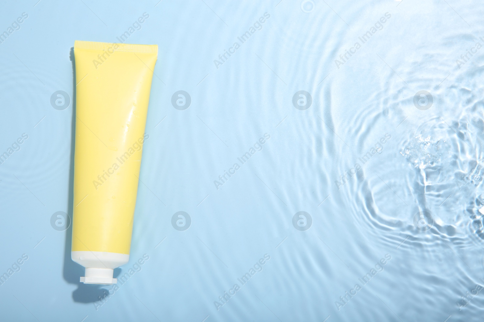 Photo of Cosmetic product. Tube with cream in water on light blue background, top view. Space for text