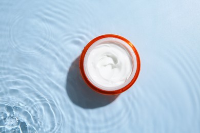 Photo of Cosmetic product. Jar with cream in water on light blue background, top view