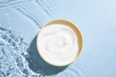 Cosmetic product. Jar with cream in water on light blue background, top view