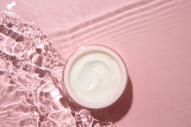 Cosmetic product. Jar with cream in water on pink background, top view