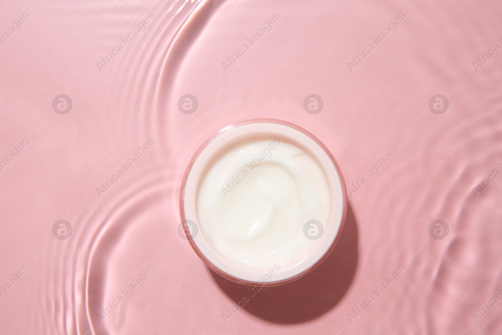 Photo of Cosmetic product. Jar with cream in water on pink background, top view