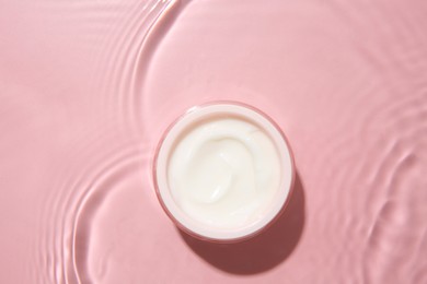 Cosmetic product. Jar with cream in water on pink background, top view