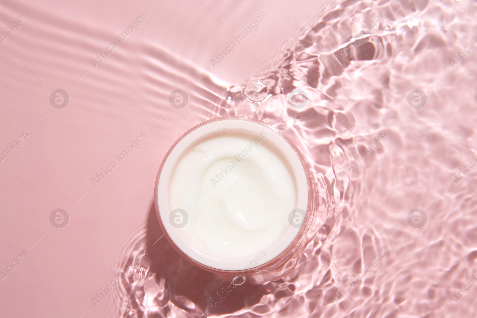 Photo of Cosmetic product. Jar with cream in water on pink background, top view