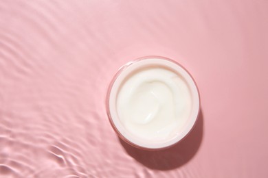 Photo of Cosmetic product. Jar with cream in water on pink background, top view