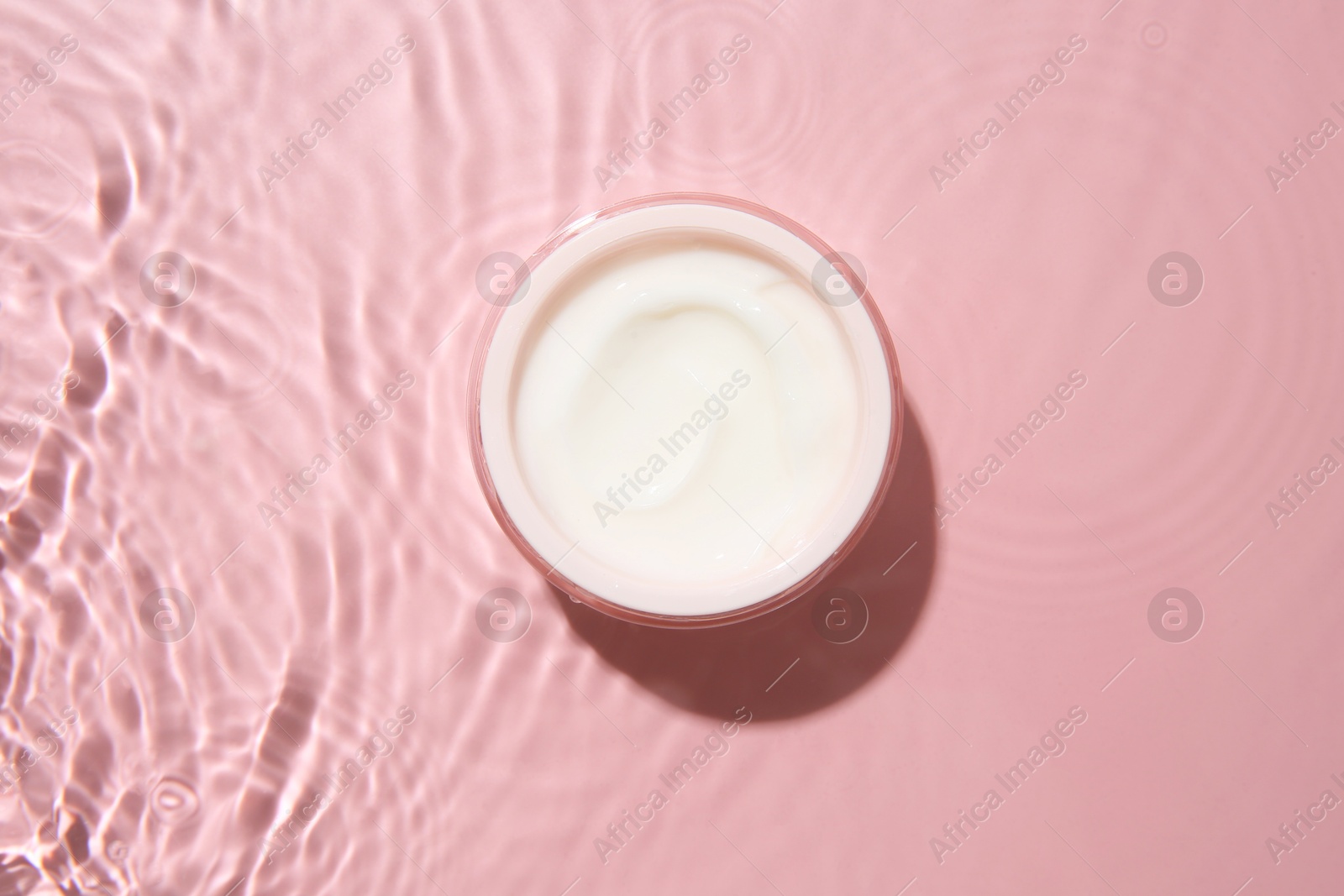 Photo of Cosmetic product. Jar with cream in water on pink background, top view