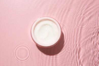 Photo of Cosmetic product. Jar with cream in water on pink background, top view