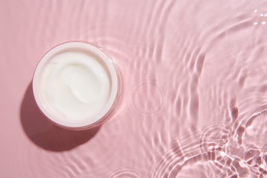 Cosmetic product. Jar with cream in water on pink background, top view. Space for text