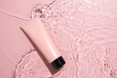 Cosmetic product. Tube with cream in water on pink background, top view. Space for text