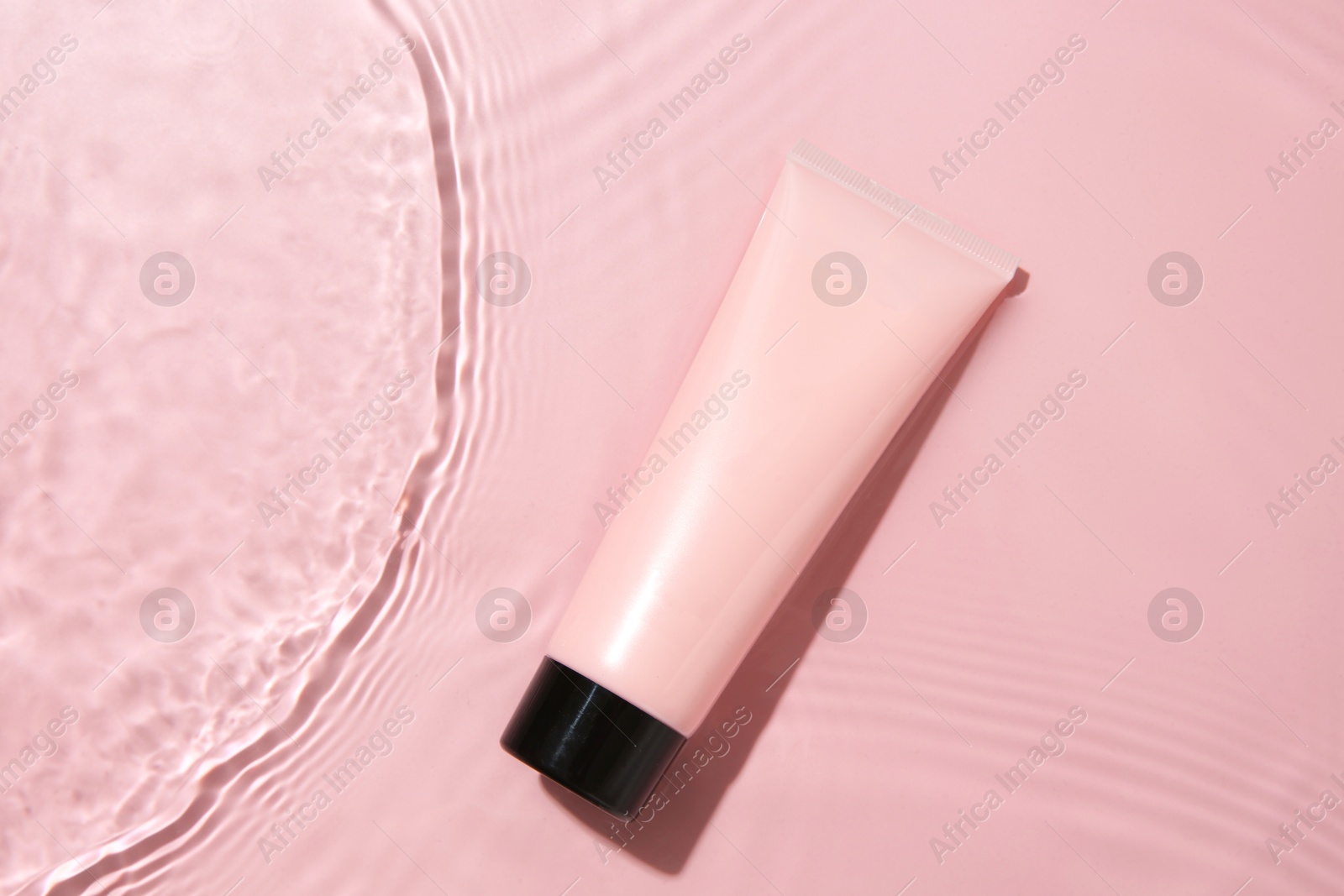 Photo of Cosmetic product. Tube with cream in water on pink background, top view