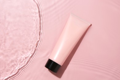 Cosmetic product. Tube with cream in water on pink background, top view