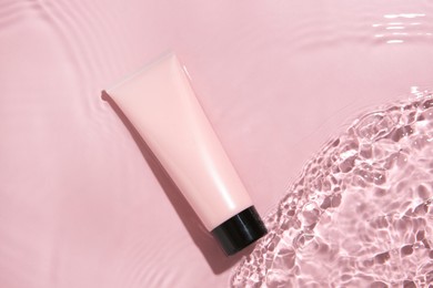 Cosmetic product. Tube with cream in water on pink background, top view