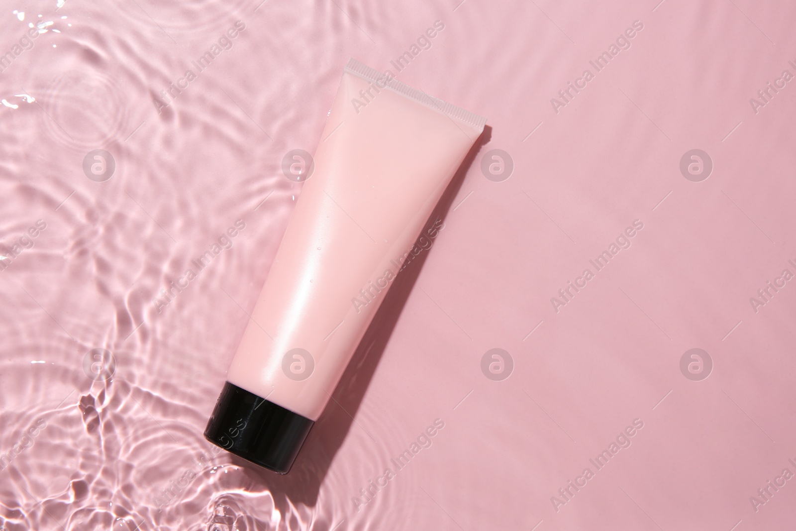 Photo of Cosmetic product. Tube with cream in water on pink background, top view