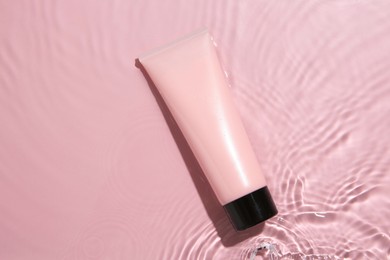 Photo of Cosmetic product. Tube with cream in water on pink background, top view